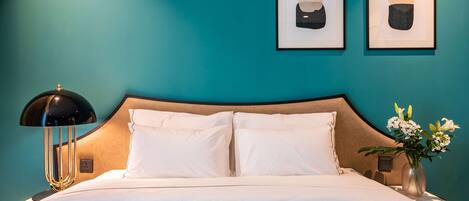 A neatly made bed with white linens, a black lamp with a gold base, and a vase with flowers on a nightstand.