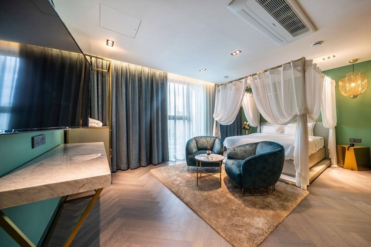 A modern bedroom with a bed, two armchairs, a small table, a vanity, and a large window with curtains.