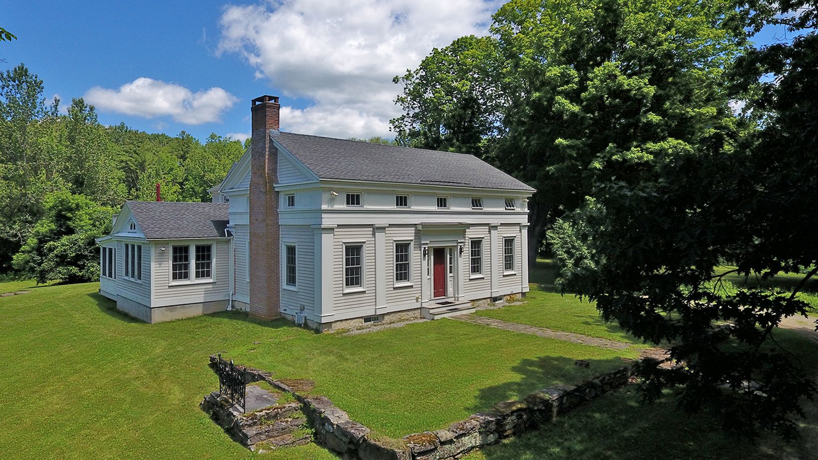 A large, single-story house with a brick chimney, a red door, and a well-maintained lawn.