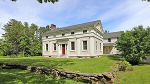 A two-story house with a red door, surrounded by a well-maintained lawn and stone wall.