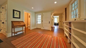 A hallway with wooden flooring, a striped rug, and a wooden bench. There are white doors and a shelf unit with baskets.