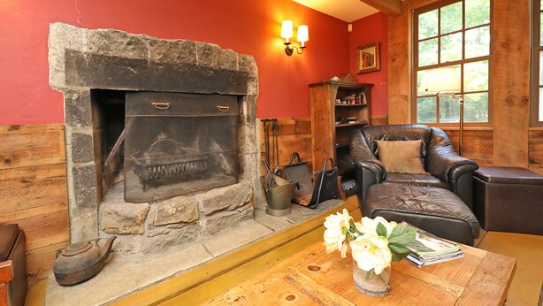 A cozy living room with a stone fireplace, leather sofa, and a wooden coffee table with flowers.