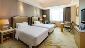 Une chambre d’hôtel avec deux lits, un bureau, une chaise, une télévision et une fenêtre avec des rideaux.