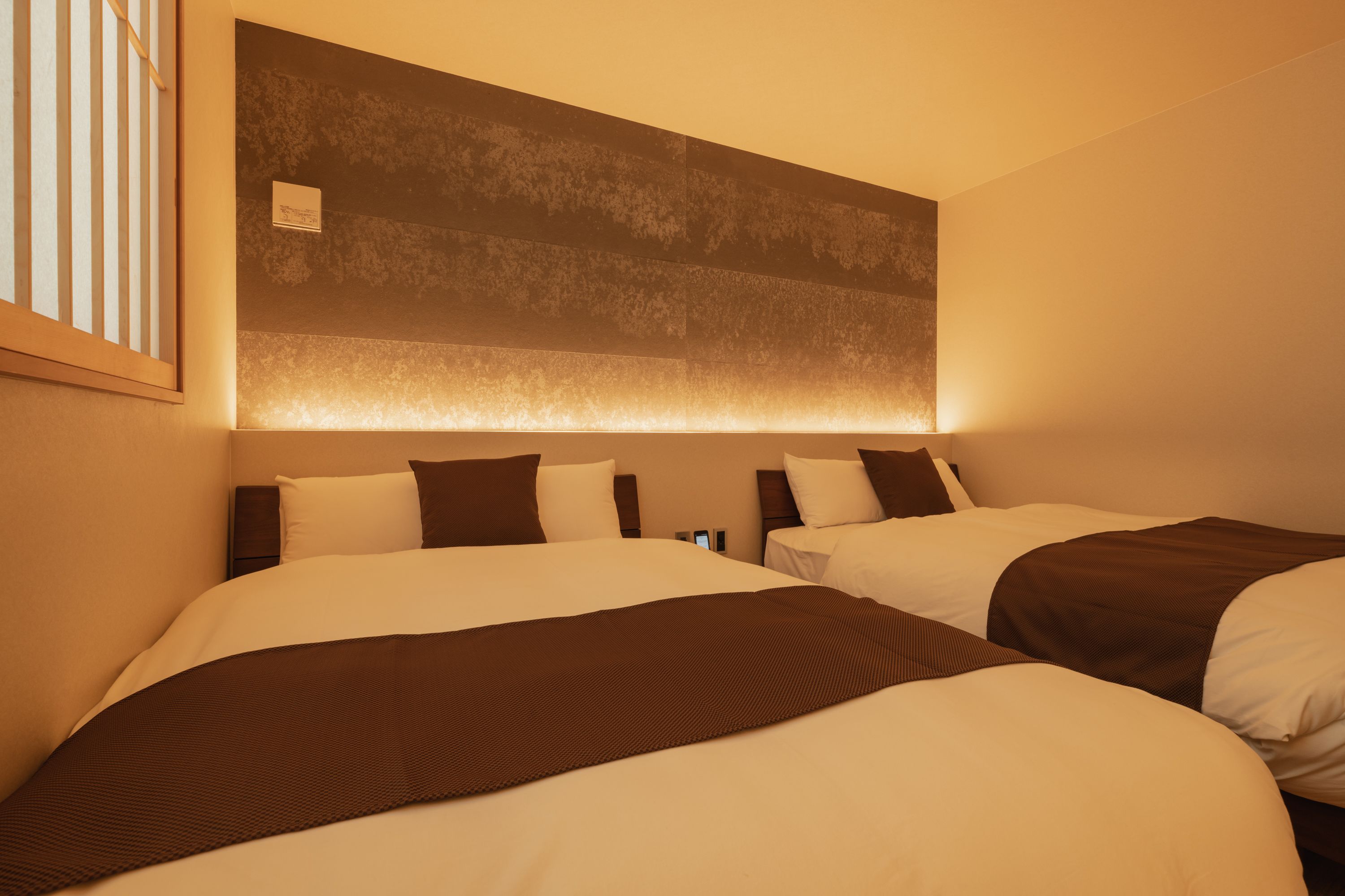 Een hotelkamer met twee bedden, elk met een bruin hoofdeinde, en een grote wandlamp boven de bedden.