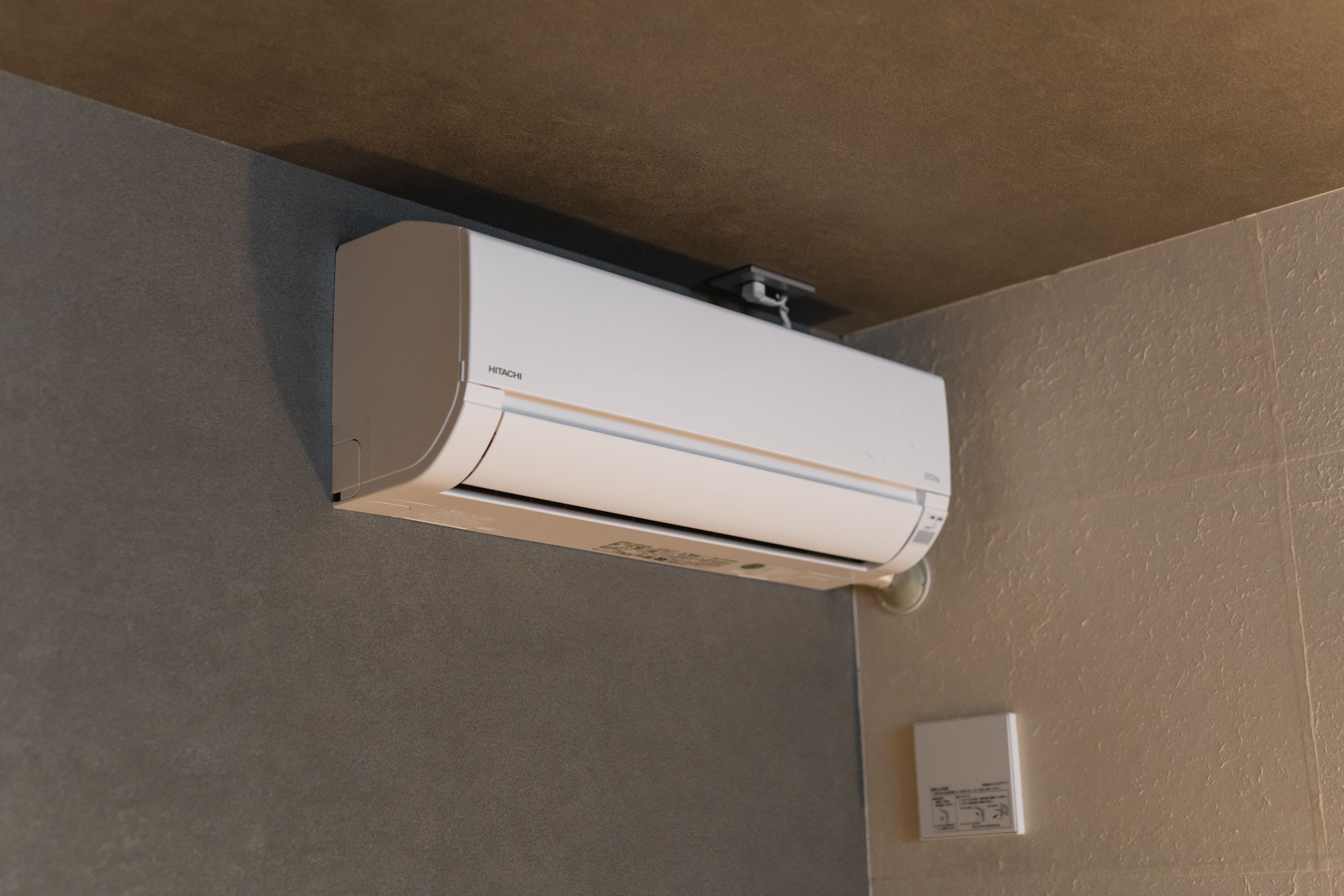 Eine Wand-Klimaanlage in einem Raum mit strukturierter Wand und sichtbarer Steckdose.