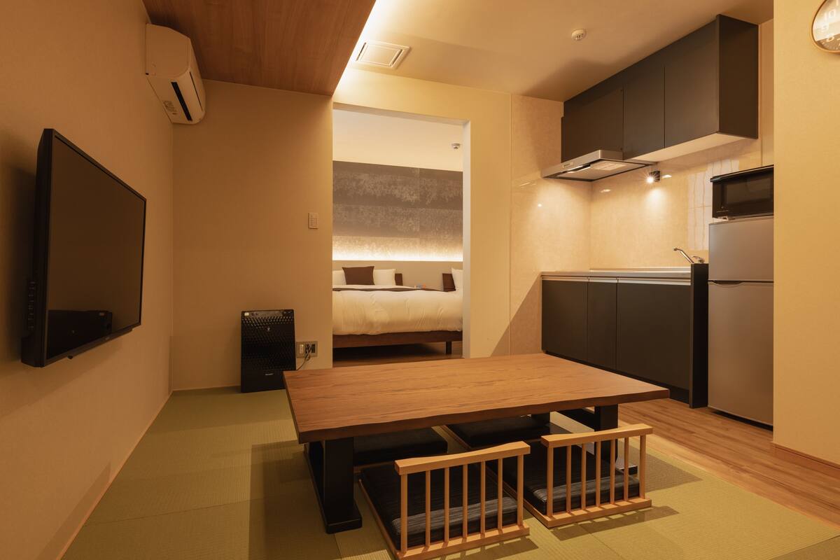 A compact living space with a bed, kitchenette, and a TV mounted on the wall.