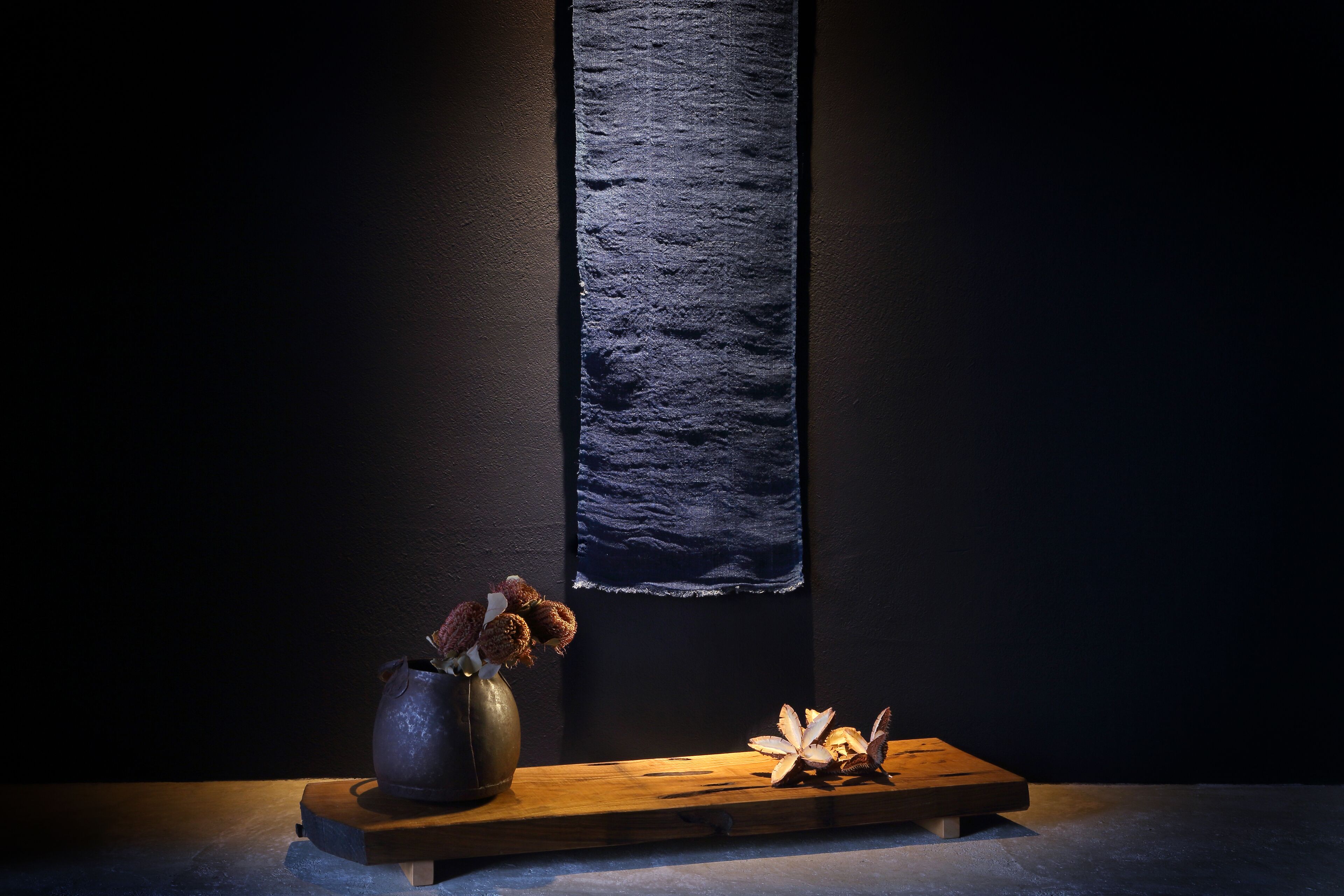 A dark room with a textured wall, a wooden table, and a vase with dried flowers.