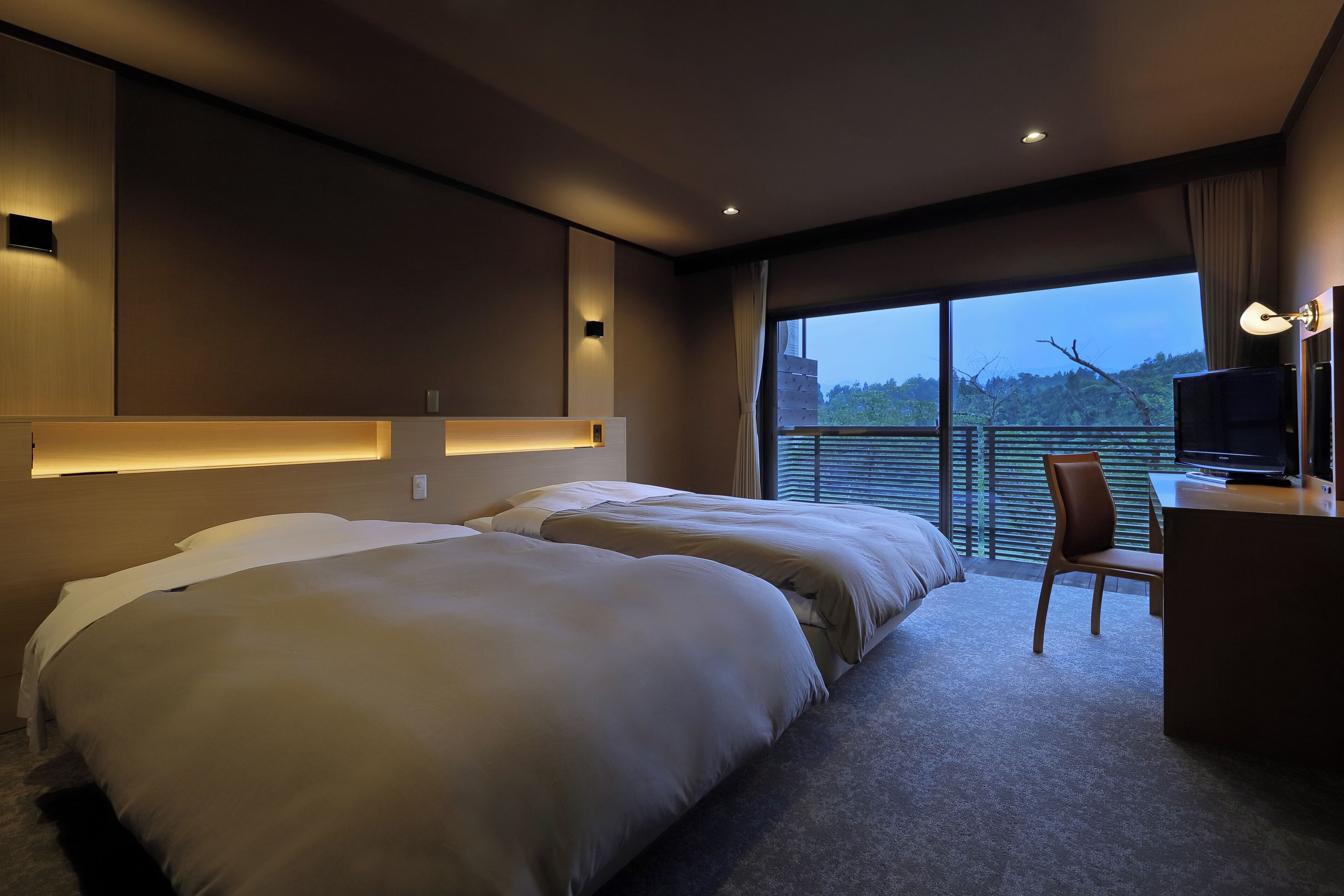 A modern hotel room with two large beds, a desk, and a view of the outdoors.