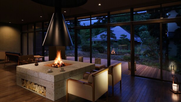 A modern outdoor seating area with a fire feature, wooden deck, and large windows offering a view of the outdoors. - Oyado Morinone - Adults Only (Kaminoyama)