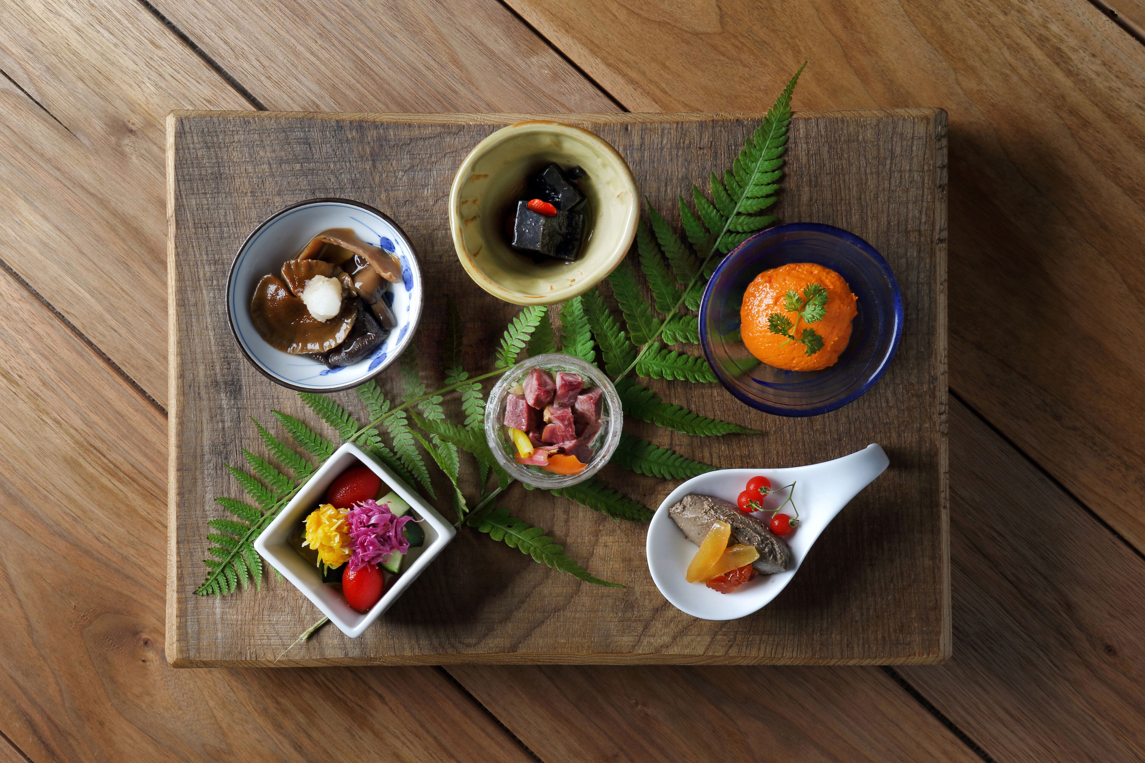 A wooden board with various food items and a small bowl of flowers.
