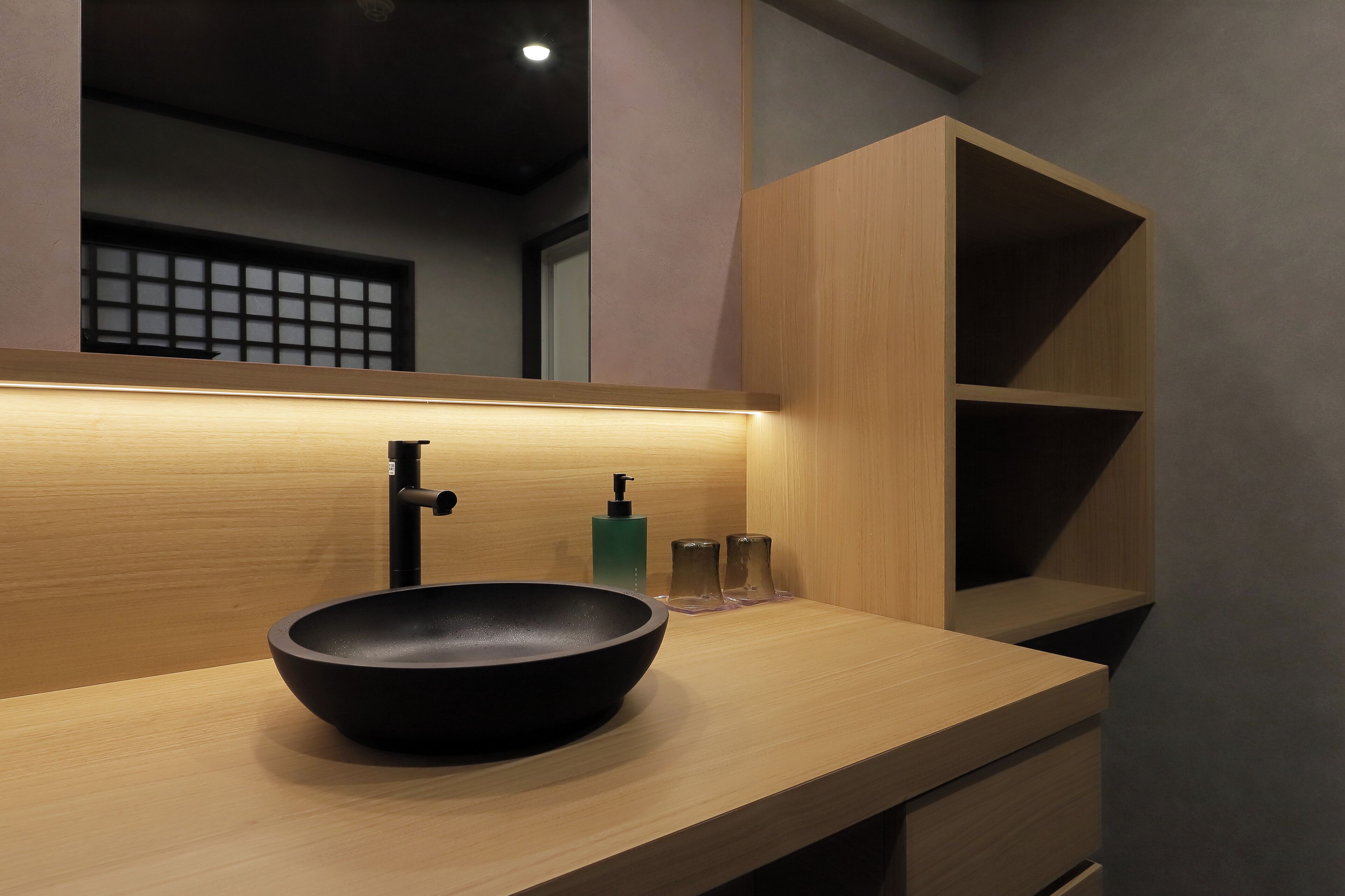 A modern bathroom with a black vessel sink, a wooden vanity, and a mirror above the sink.