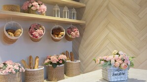 A kitchen with wooden shelves holding baskets of bread and flowers, a marble table, and a herringbone-patterned wall. - Stellar Potter's Ridge (Laurel)