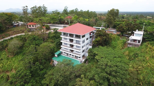 A multi-story building with a red roof, surrounded by dense greenery.