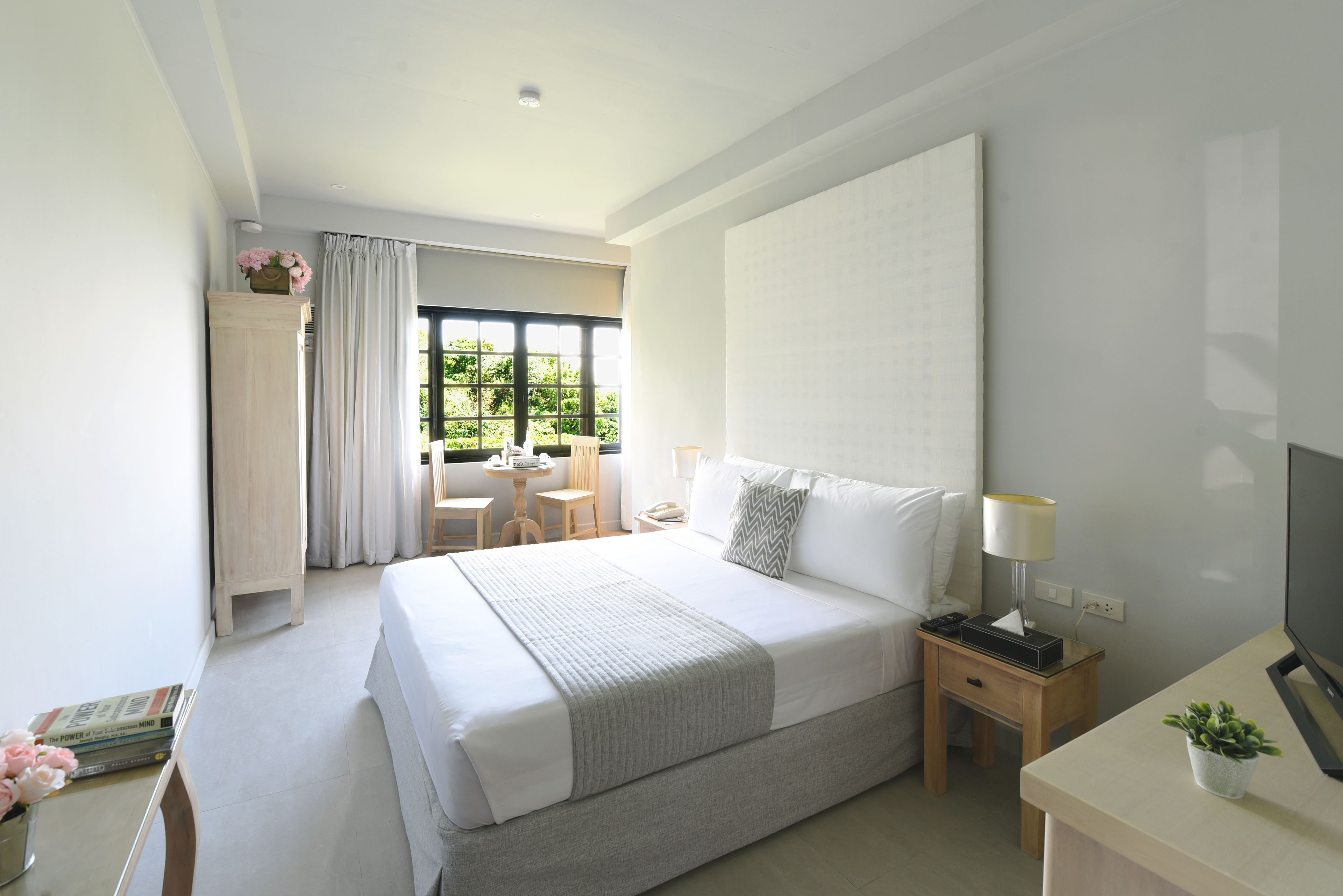 Une chambre d’hôtel moderne avec un grand lit, une table de chevet avec une lampe, une télévision et une petite table avec une plante.