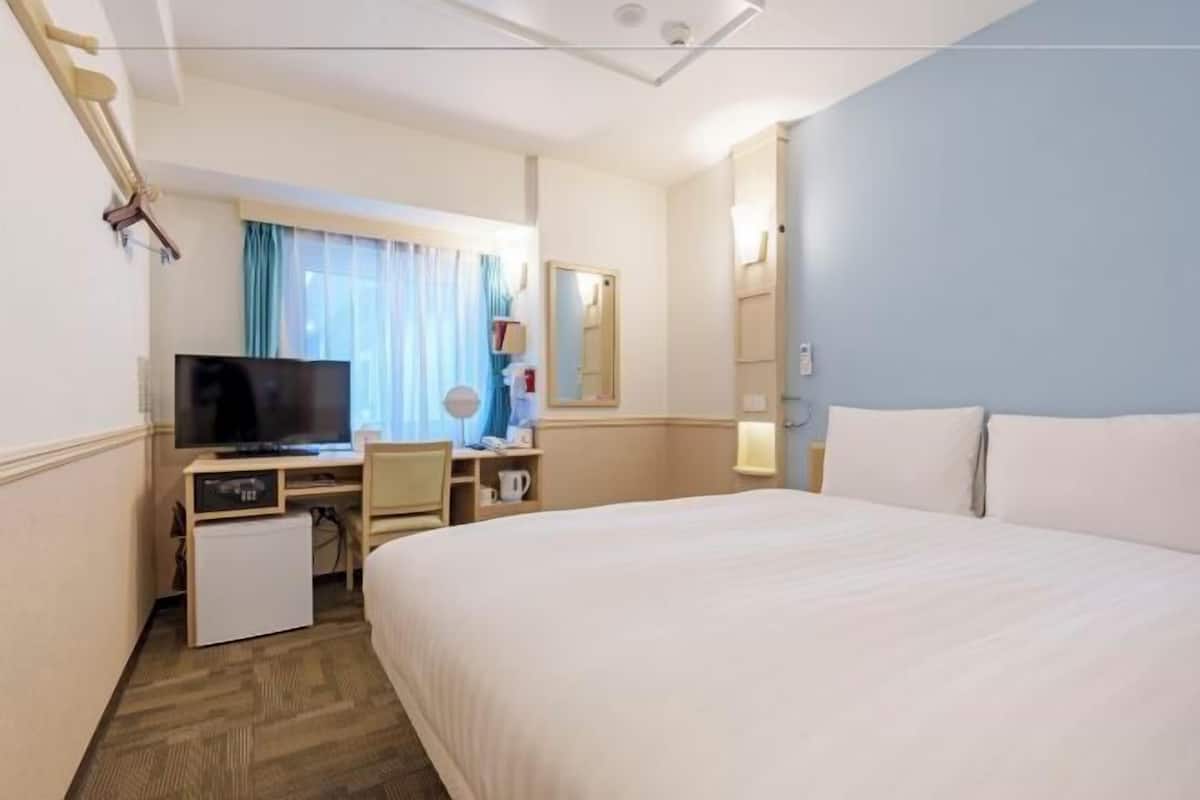A hotel room with a bed, a desk with a television, a small refrigerator, and a mirror.