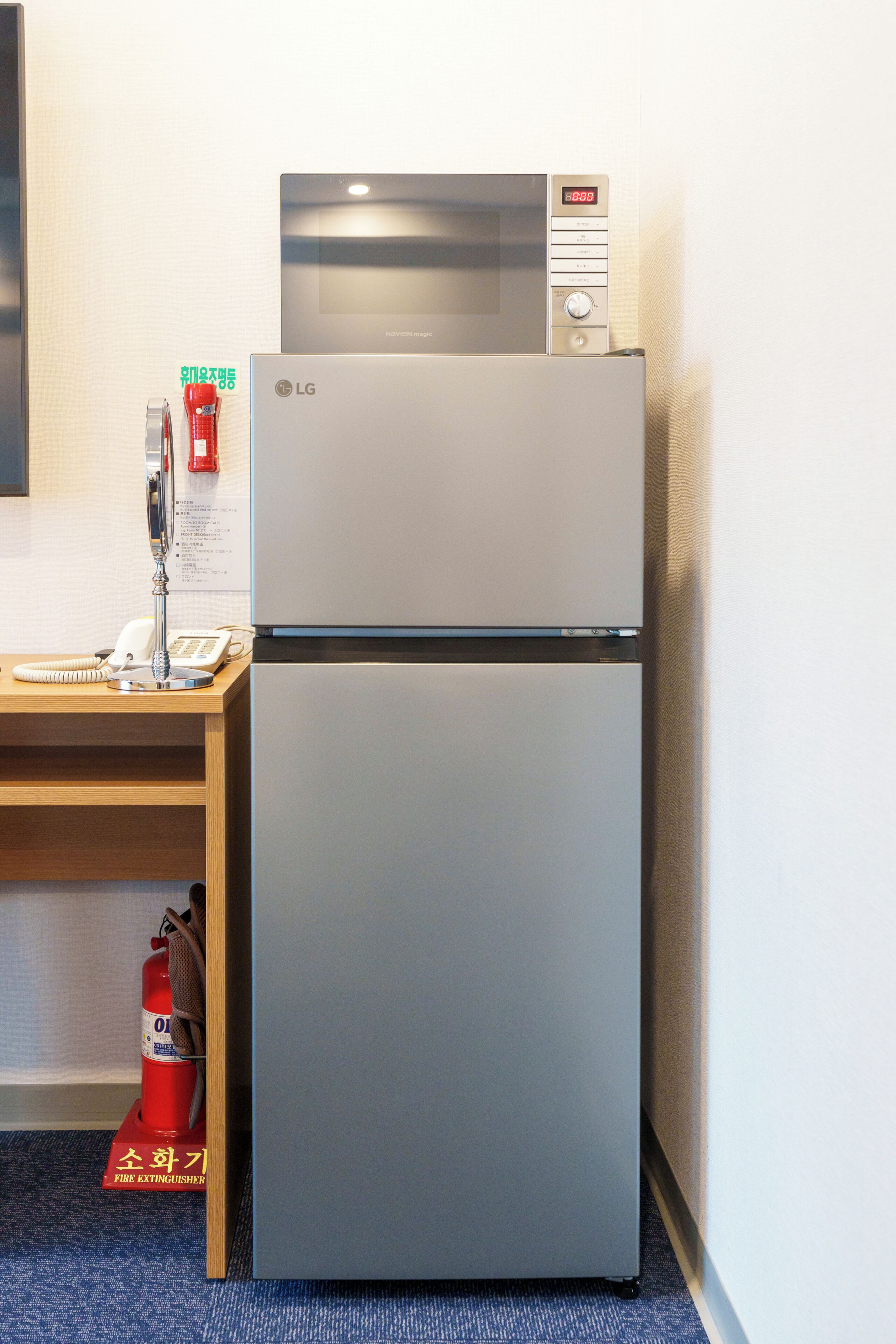 A modern kitchen with a built-in microwave and refrigerator, a wooden desk with a telephone, and a fire extinguisher on the floor.