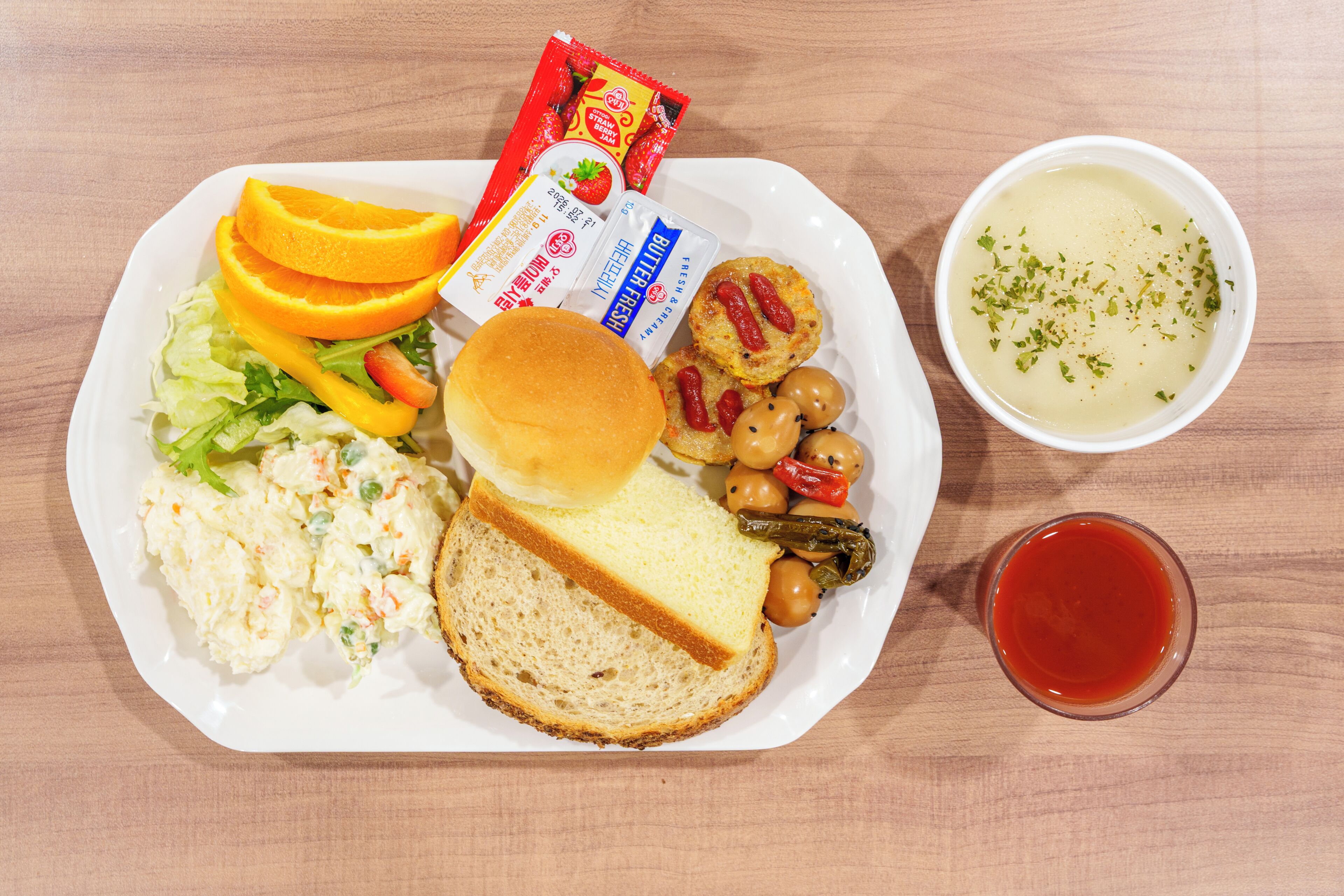 A meal with bread, salad, fruit, and soup on a plate.