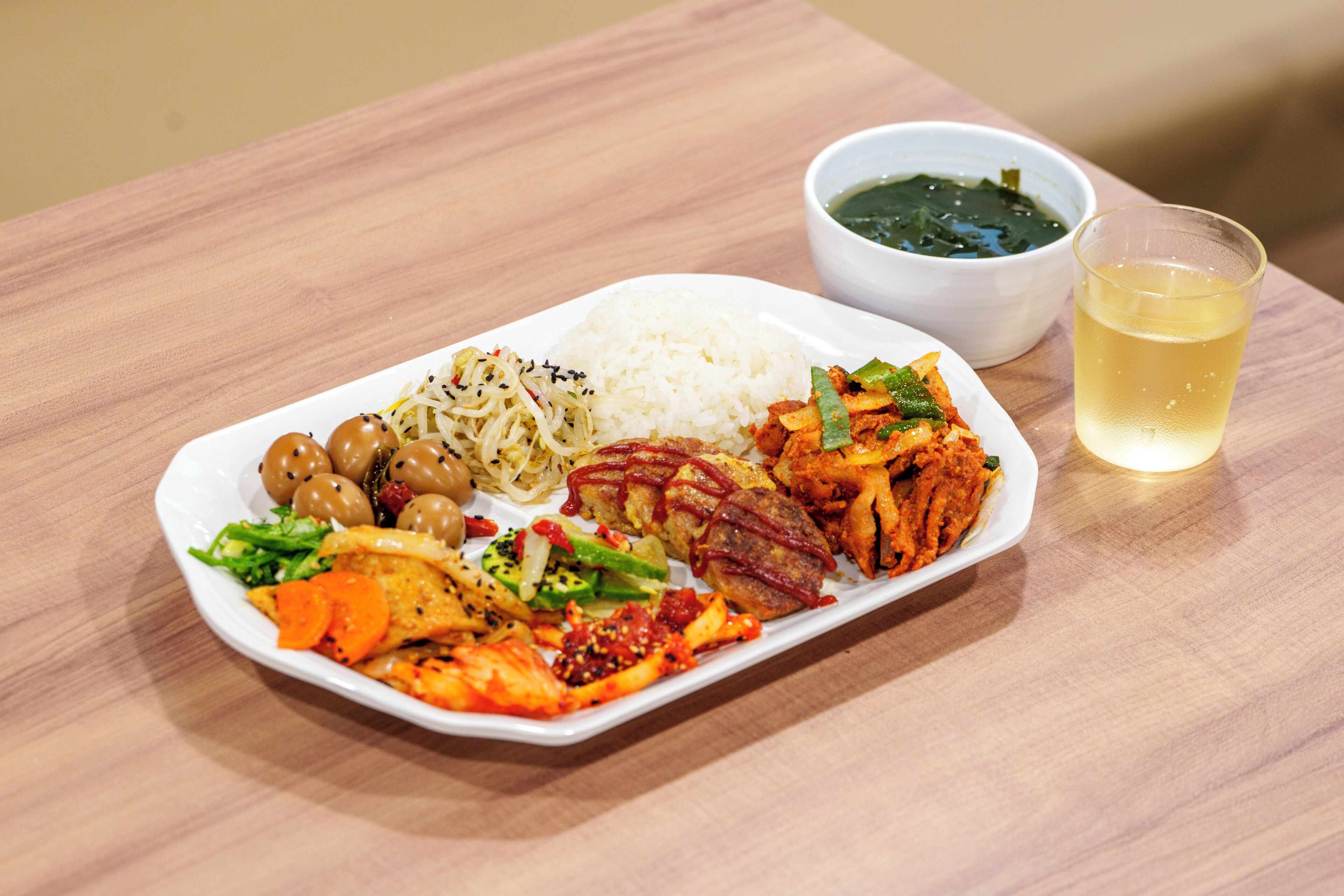 Un plato de comida con arroz, verduras y un tazón de sopa sobre una mesa de madera.