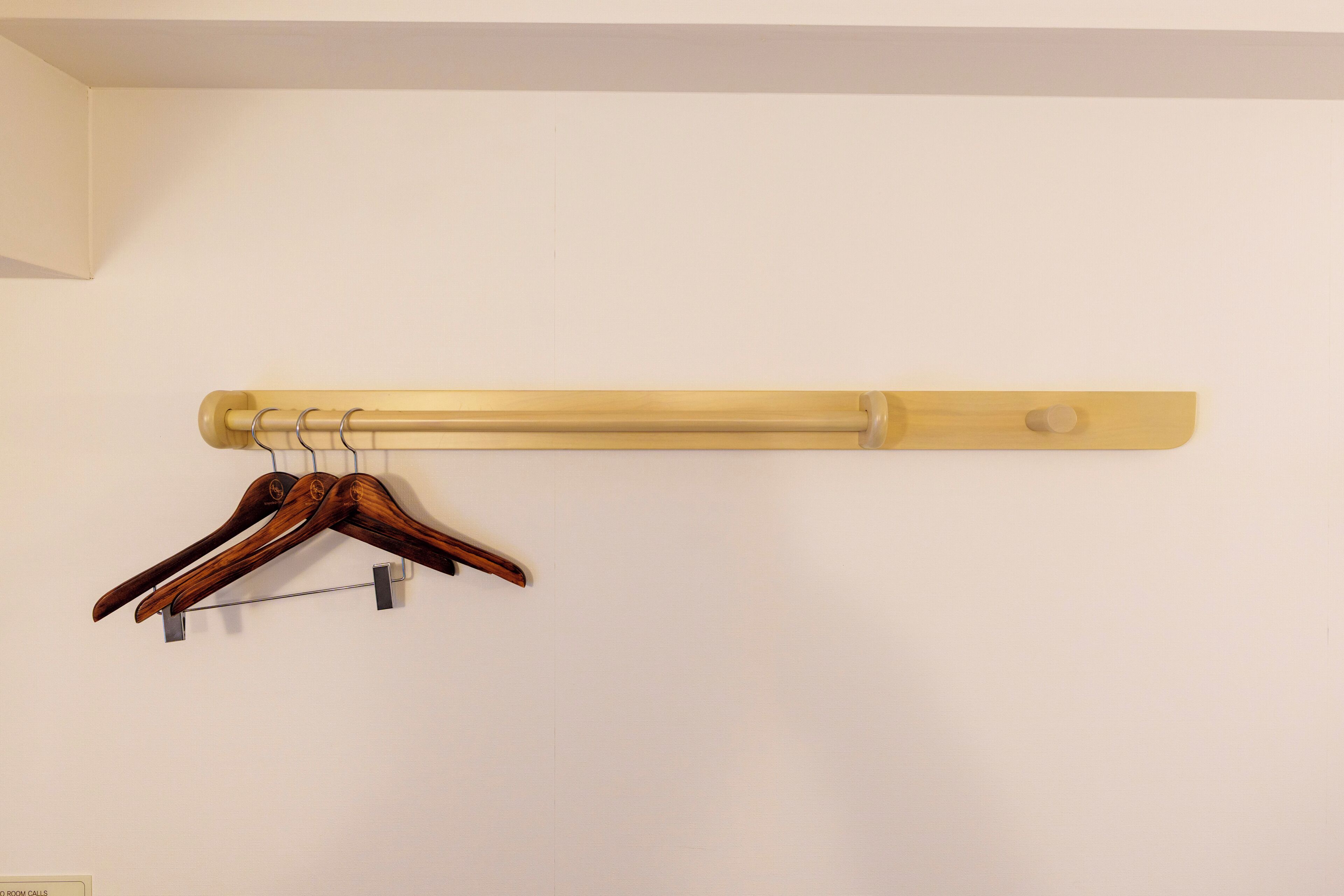 Un porte-manteau en bois, muni de trois patères, est adossé à un mur uni.