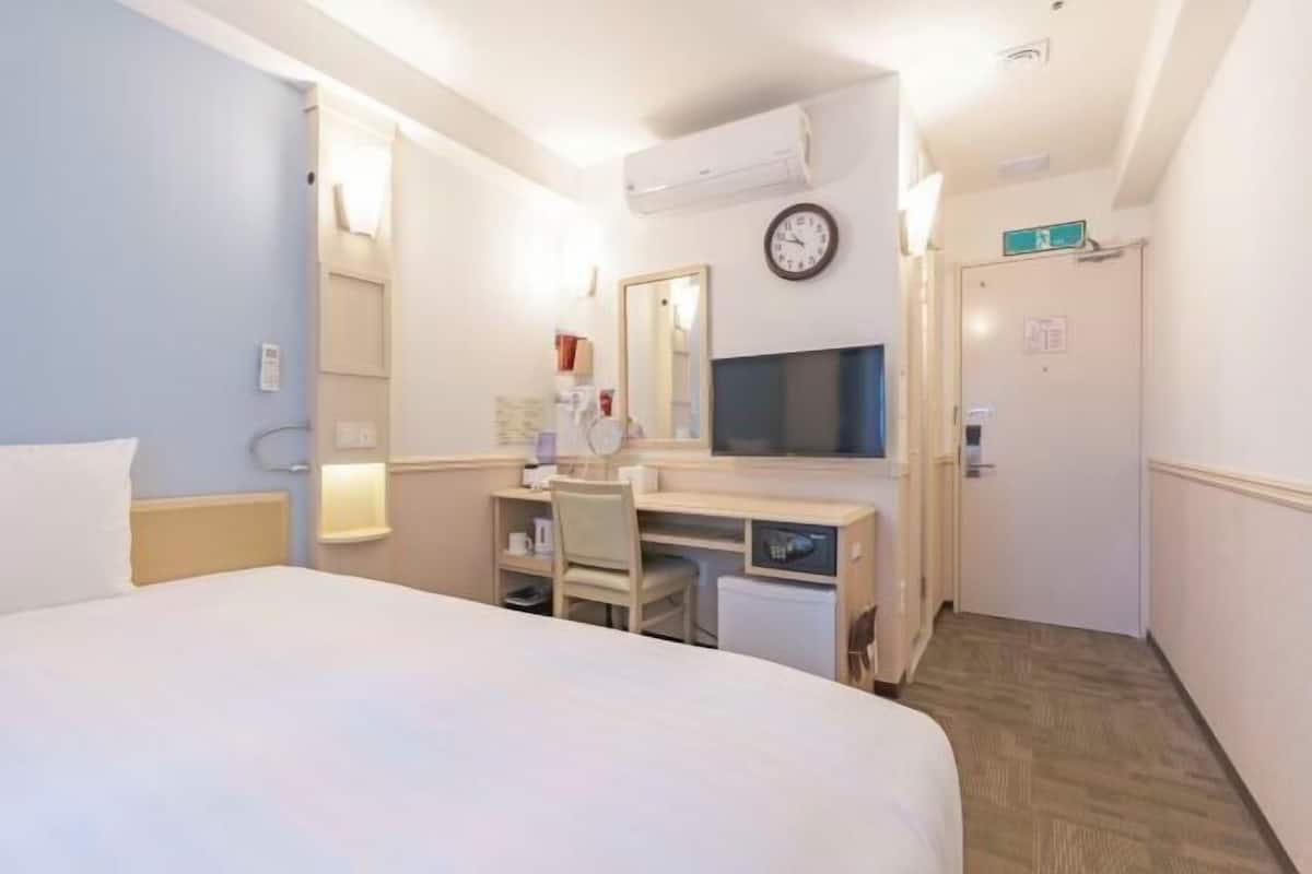 A hotel room with a bed, desk, chair, TV, and a clock on the wall.