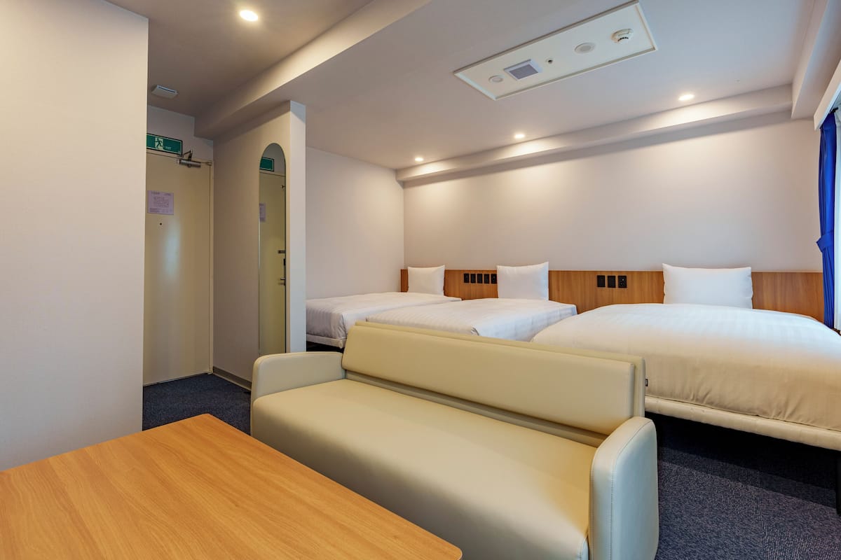 A hotel room with two beds, a sofa, a wooden table, and a mirror.