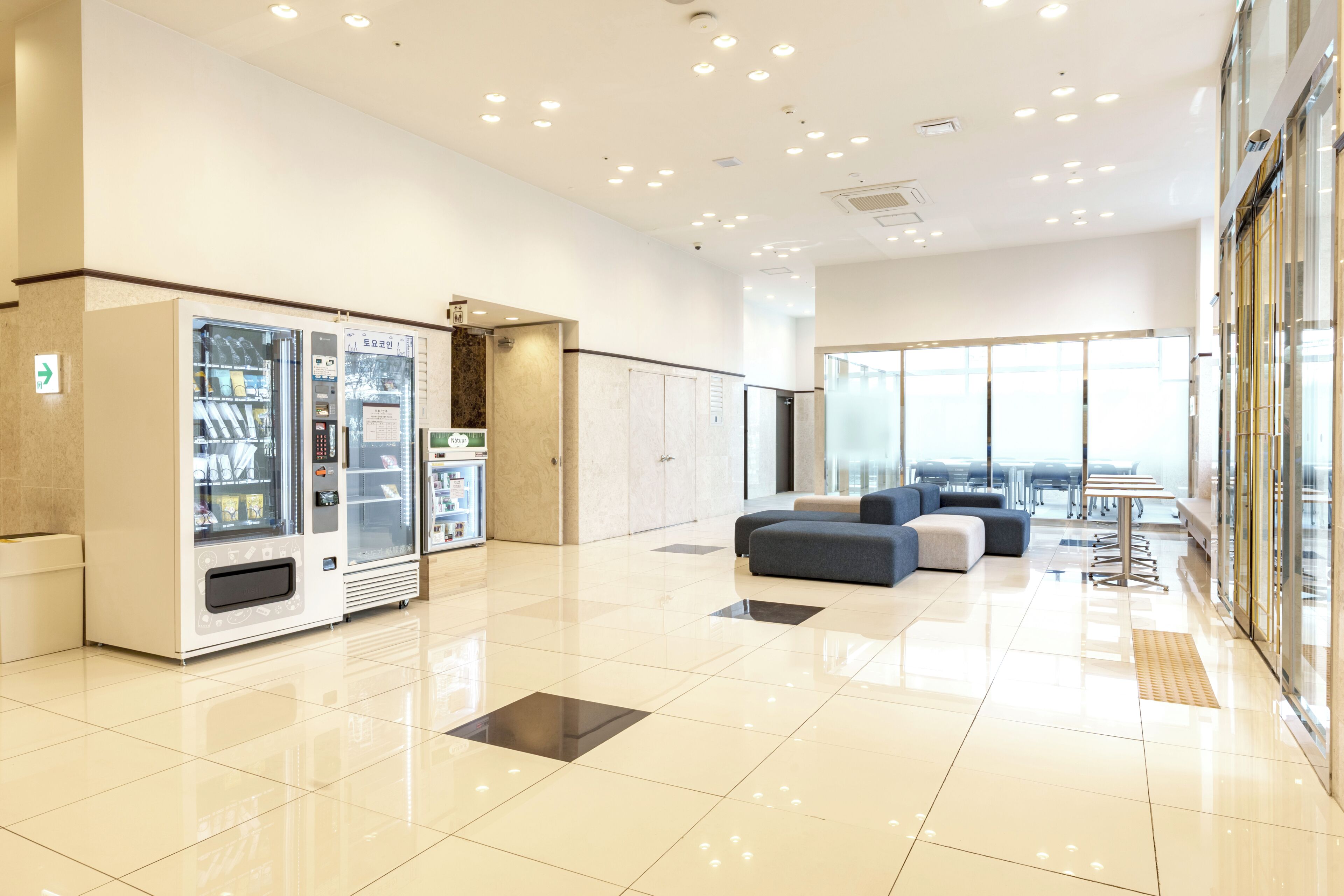 Um lobby moderno com máquinas de venda automática, áreas de estar e vista através de amplas janelas.