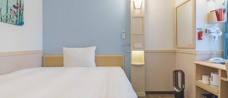 A hotel room with a bed, a bedside table with a lamp, a mirror, a hairdryer, and a trash bin.