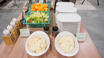 A buffet table with various dishes, including salads and a sweet salad, and a stack of white plates.