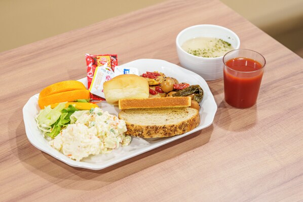 Un plato con comida que incluye pan, ensalada y sopa, y un vaso de jugo de tomate sobre una mesa de madera.