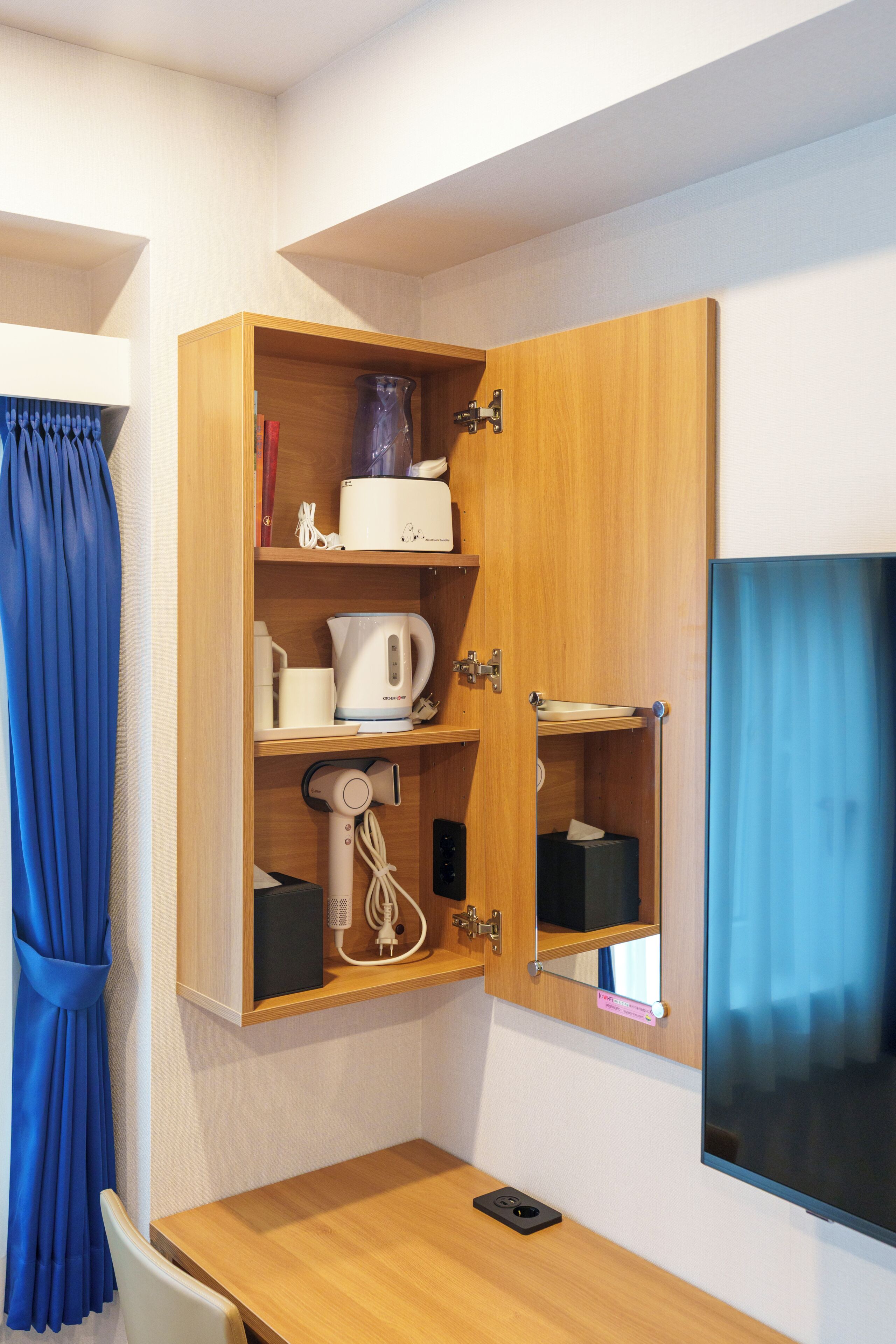 A small room with a wooden cabinet containing a kettle, a hairdryer, and a small mirror.
