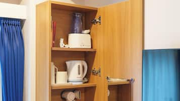 A small room with a wooden cabinet containing a kettle, a hairdryer, and a small mirror.