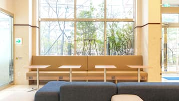 A seating area with a bench and tables, large windows with a view of trees, and a door with an arrow sign.