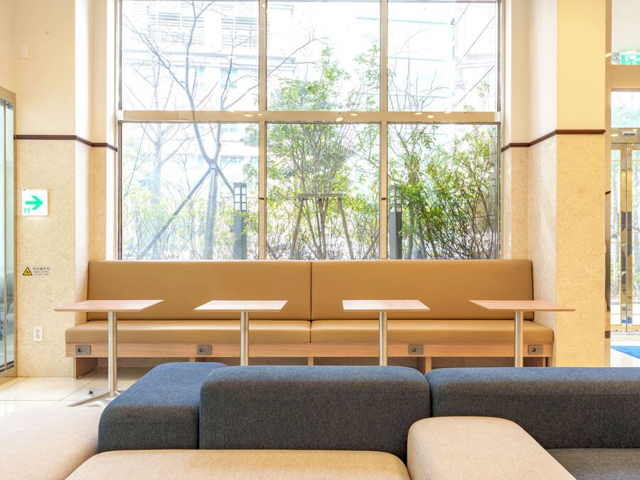 A seating area with a bench and tables, large windows with a view of trees, and a door with an arrow sign.