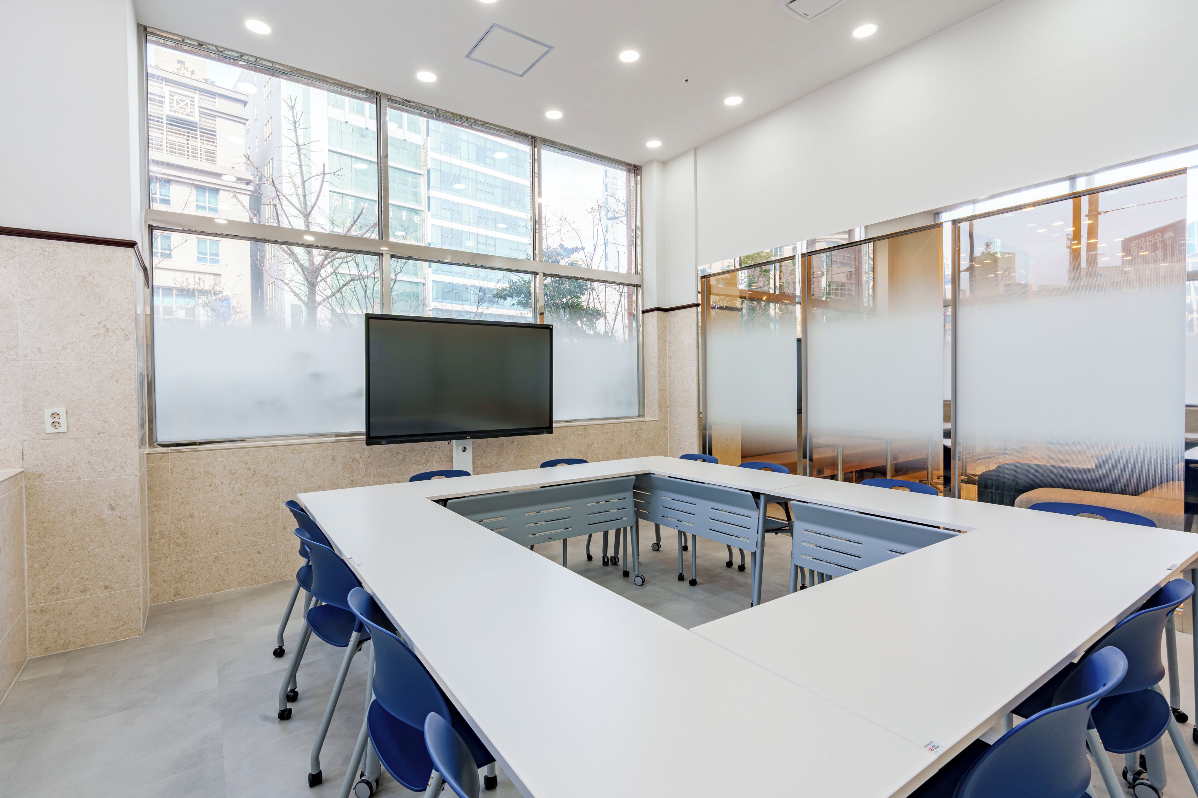 A conference room with a large table, chairs, a TV screen, and large windows.