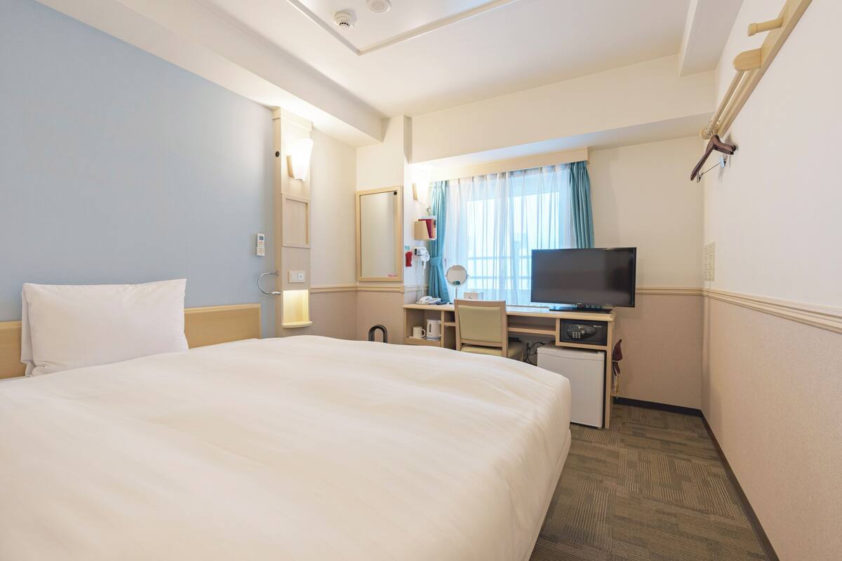 A hotel room with a bed, desk, television, and a window with curtains.