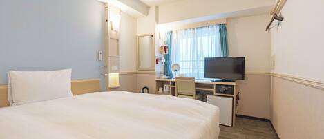 Habitación de hotel con cama, escritorio, televisor y ventana con cortinas.