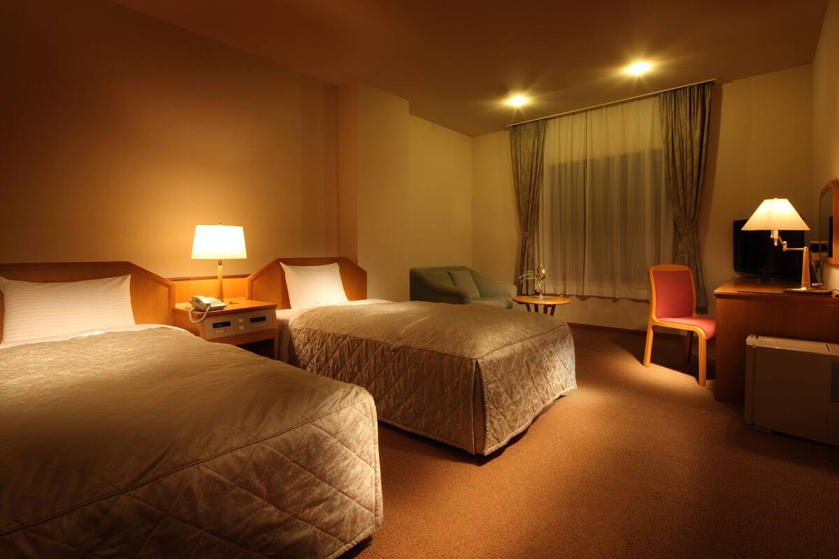 Hotellihuone, jossa on kaksi sänkyä, työpöytä, tuoli, televisio ja lämmitin.