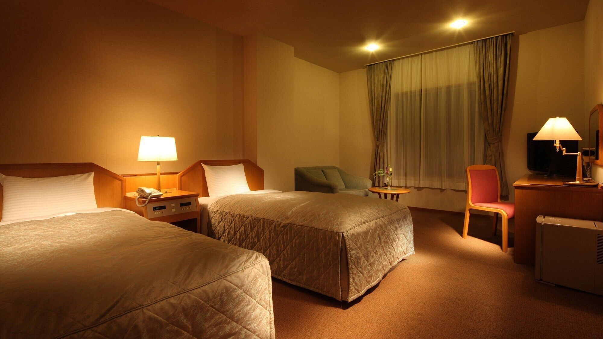 Une chambre d’hôtel avec deux lits, un bureau, une chaise, une télévision et un radiateur.