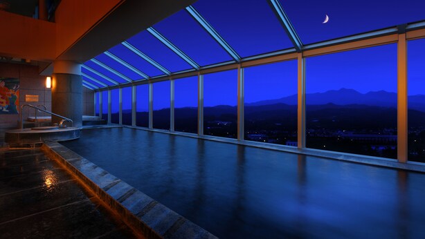 Une grande piscine intérieure dotée d’un toit en verre, offrant une vue sur les montagnes et un croissant de lune.