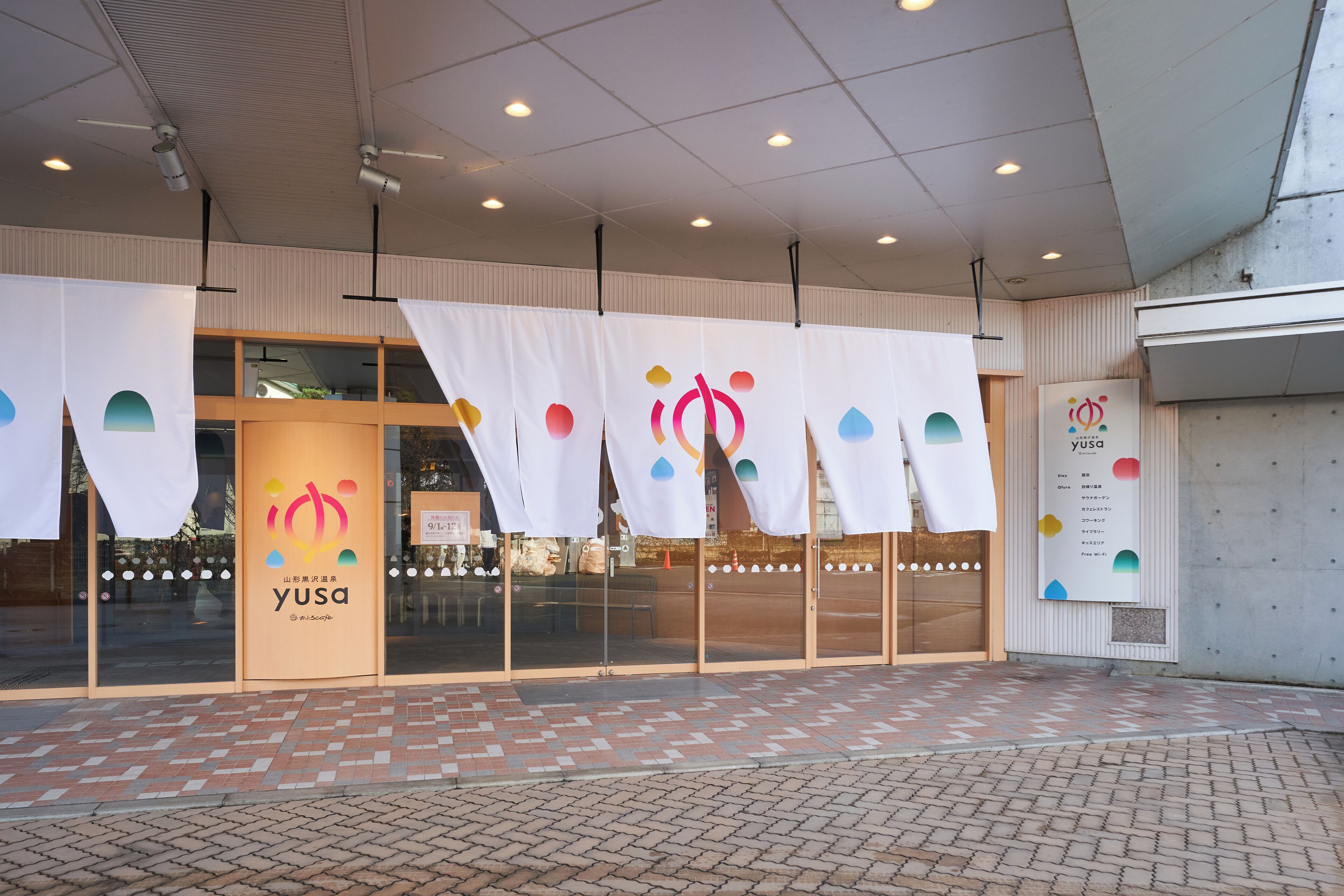 A storefront with a glass facade, a brick-patterned entrance, and a sign with the logo 'yusa'.
