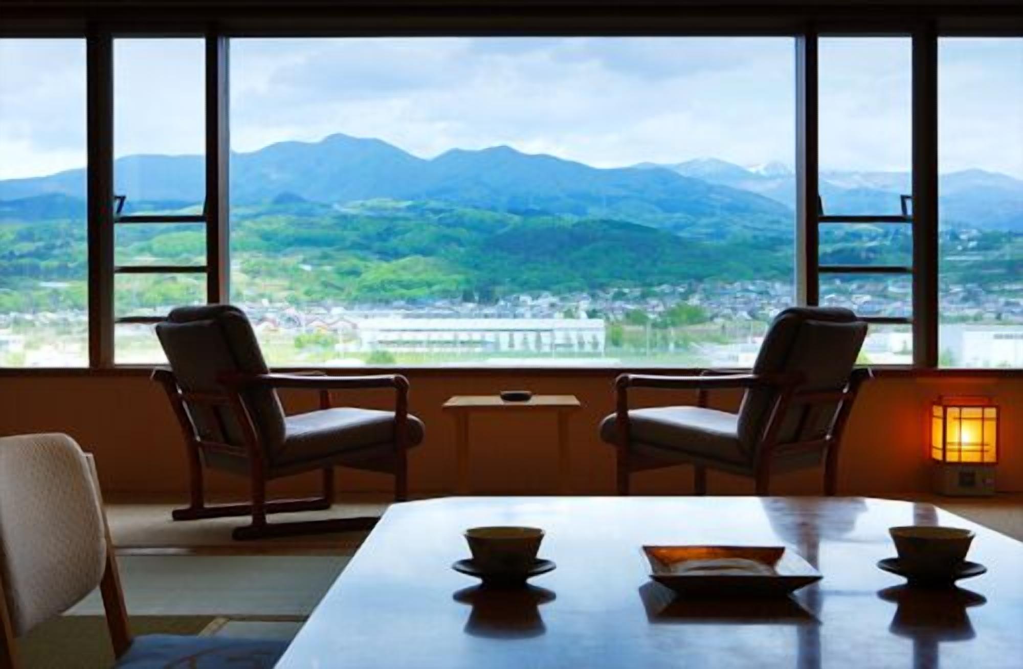 Une pièce avec une table, deux chaises et une vue sur les montagnes, visible à travers de grandes fenêtres.