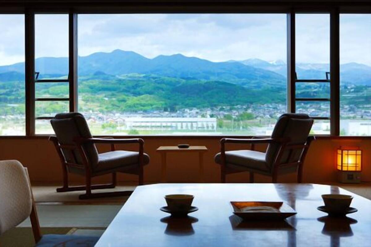 Una habitación con una mesa, dos sillas y vistas a montañas a través de amplios ventanales.