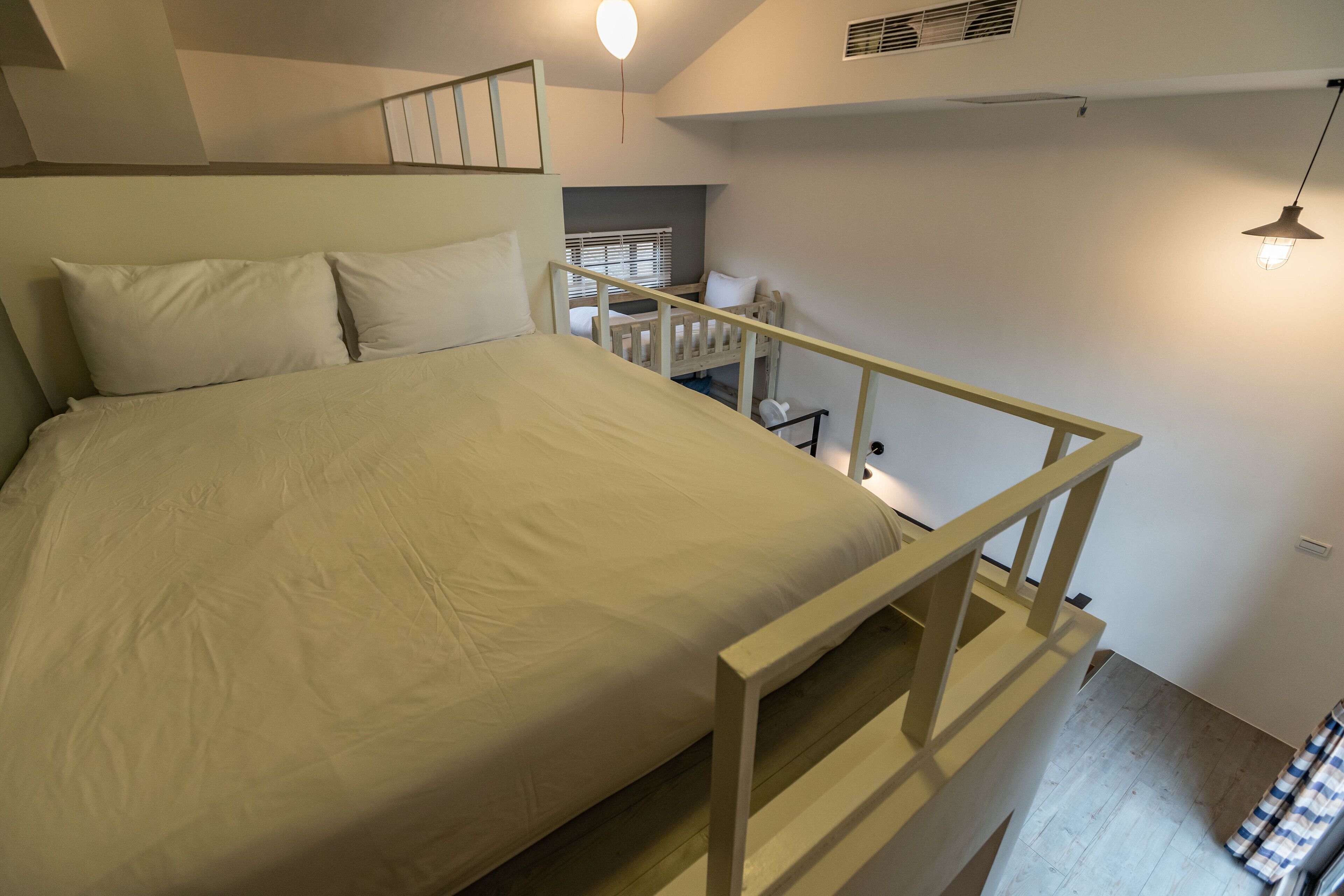 A bedroom with a bed, a wooden headboard, a staircase, and a hanging light fixture.