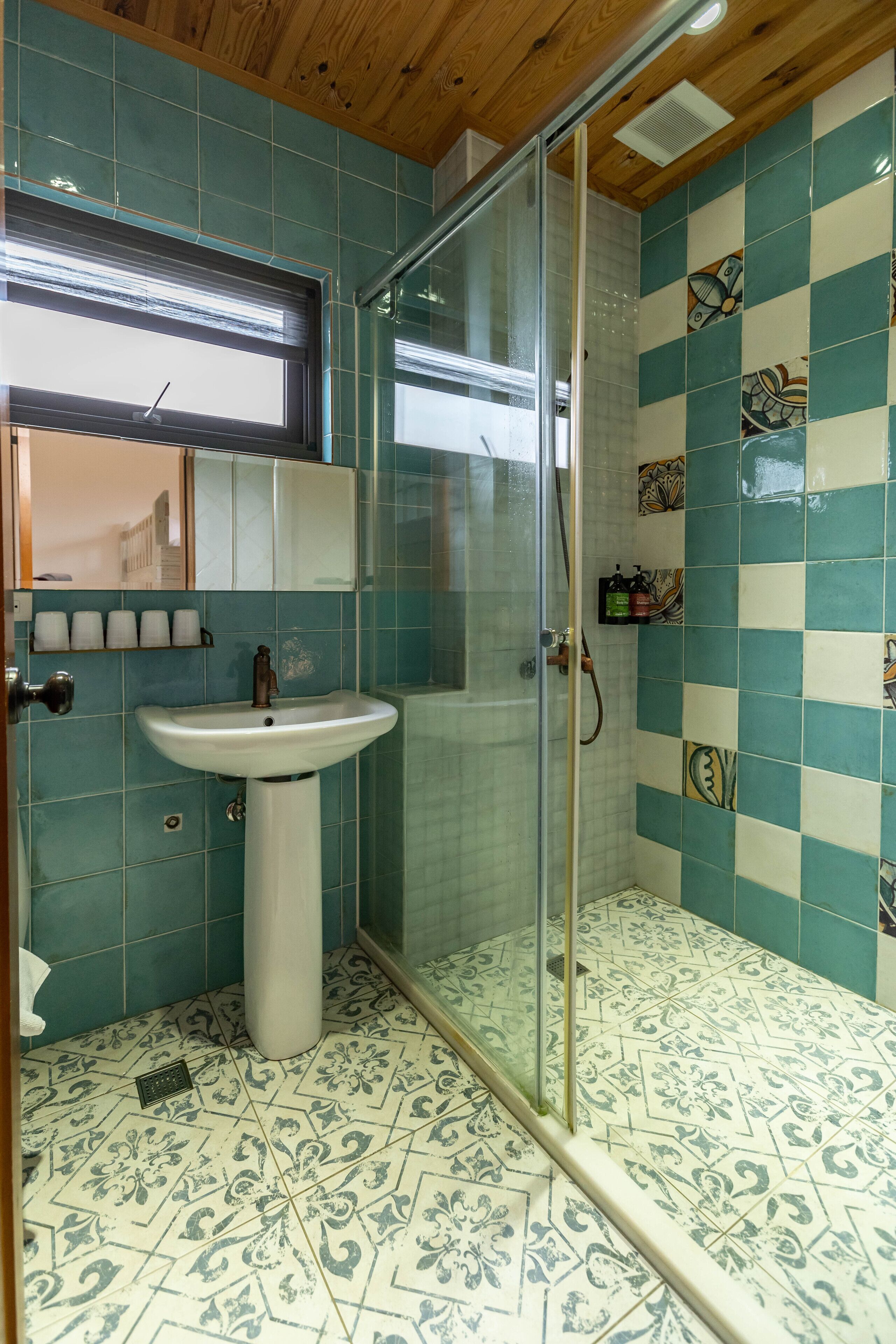 A bathroom with a glass shower enclosure, a sink, and decorative tiles.