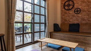 A modern living room with a large sliding glass door, a wooden table, blue cushioned seating, and a brick wall with decorative wheels. - Forest B&B (Ji'an)