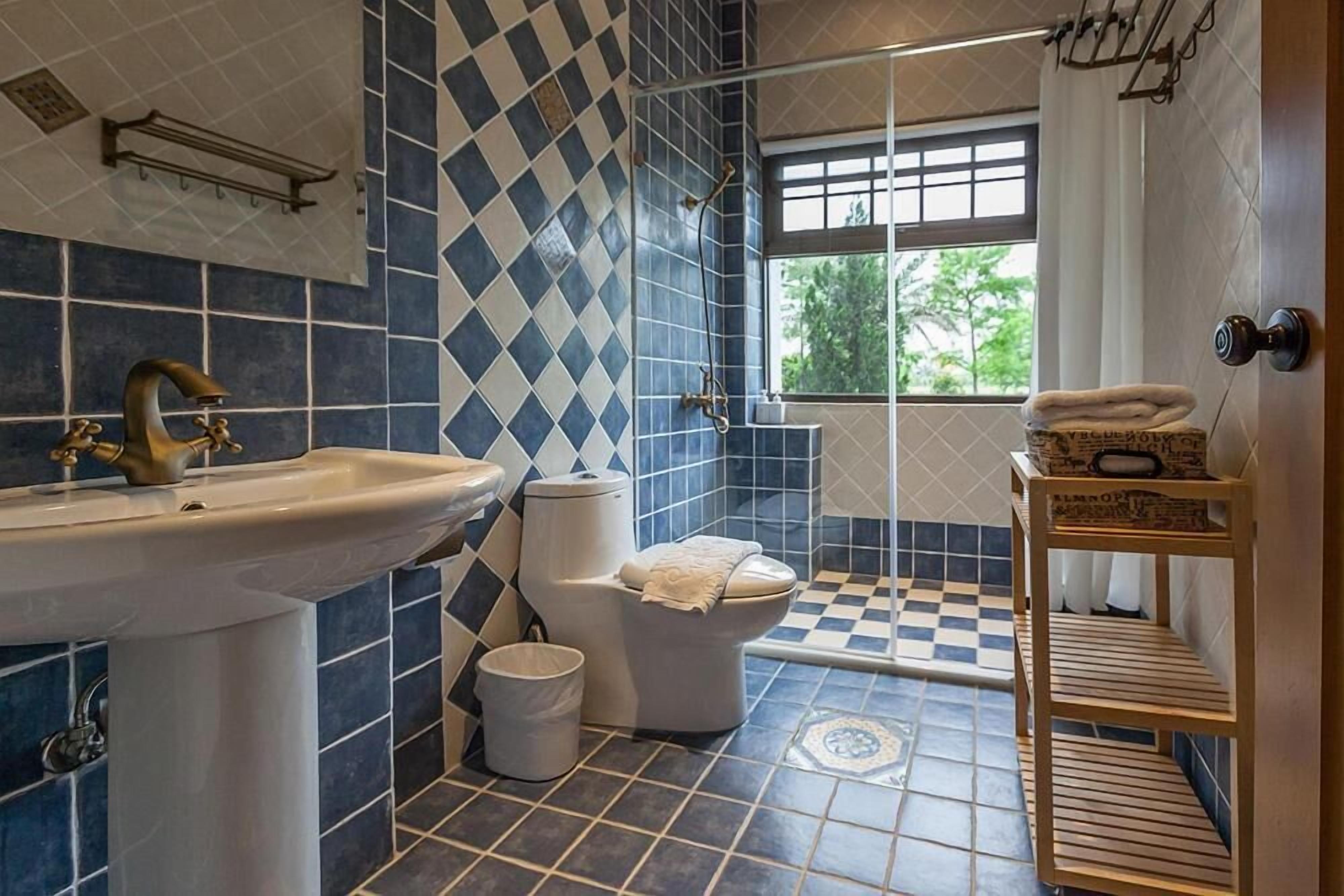 Un baño con lavamanos, inodoro y ducha. Hay una ventana que proporciona luz natural y vistas a la vegetación exterior.