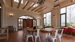 A spacious dining area with a large wooden table and white chairs, a kitchen area with modern appliances, and large windows offering views of the outdoors. - Forest B&B (Ji'an)