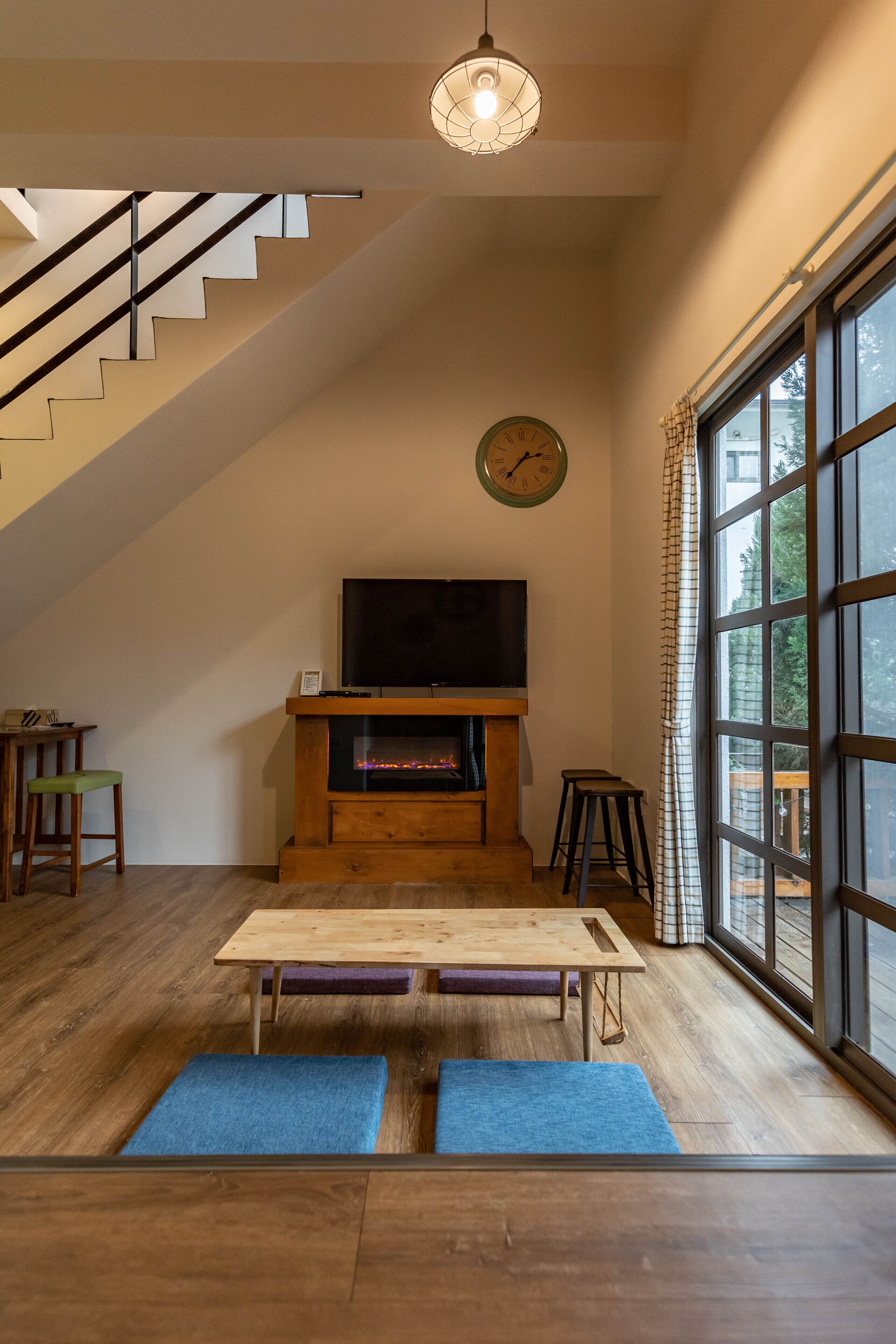 Ein modernes Wohnzimmer mit einer Holztreppe, einem Kamin, einem Fernseher und großen Fenstern.