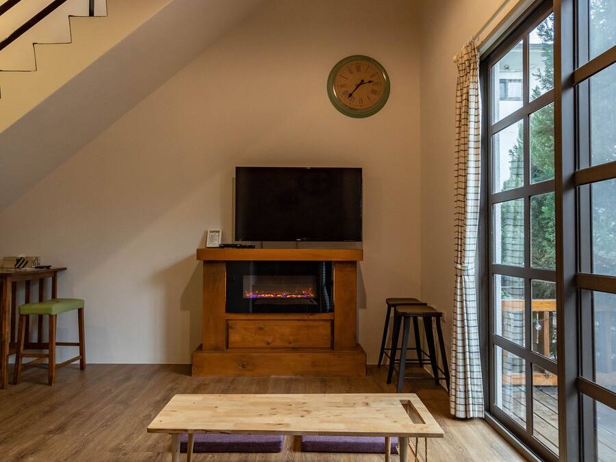 Ein modernes Wohnzimmer mit einer Holztreppe, einem Kamin, einem Fernseher und großen Fenstern.