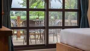 A room with a large window, a bed, and a view of an outdoor deck with chairs and a wooden fence. - Forest B&B (Ji'an)